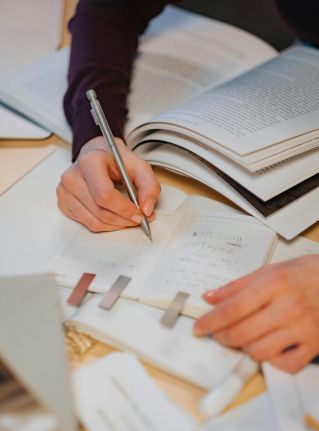 Close-up of hands writing notes in a study environment with open books.